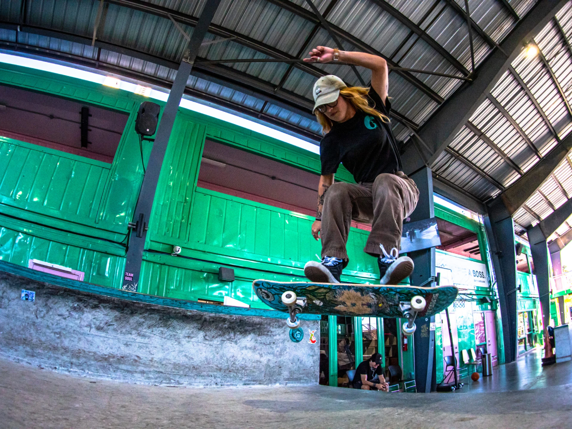 Female skateboarder mid-air performing trick inside indoor skate facility.