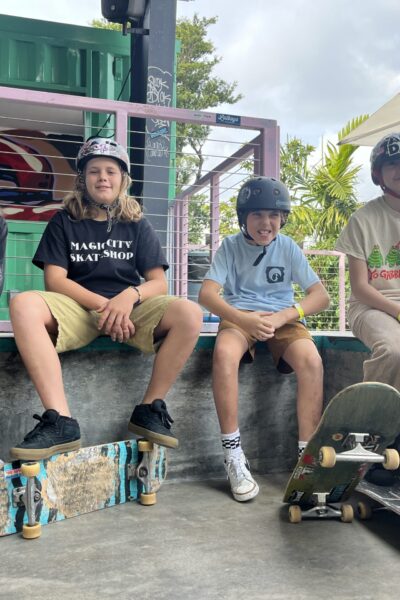 Four young skateboarders with helmets sit together on a ramp with their boards.