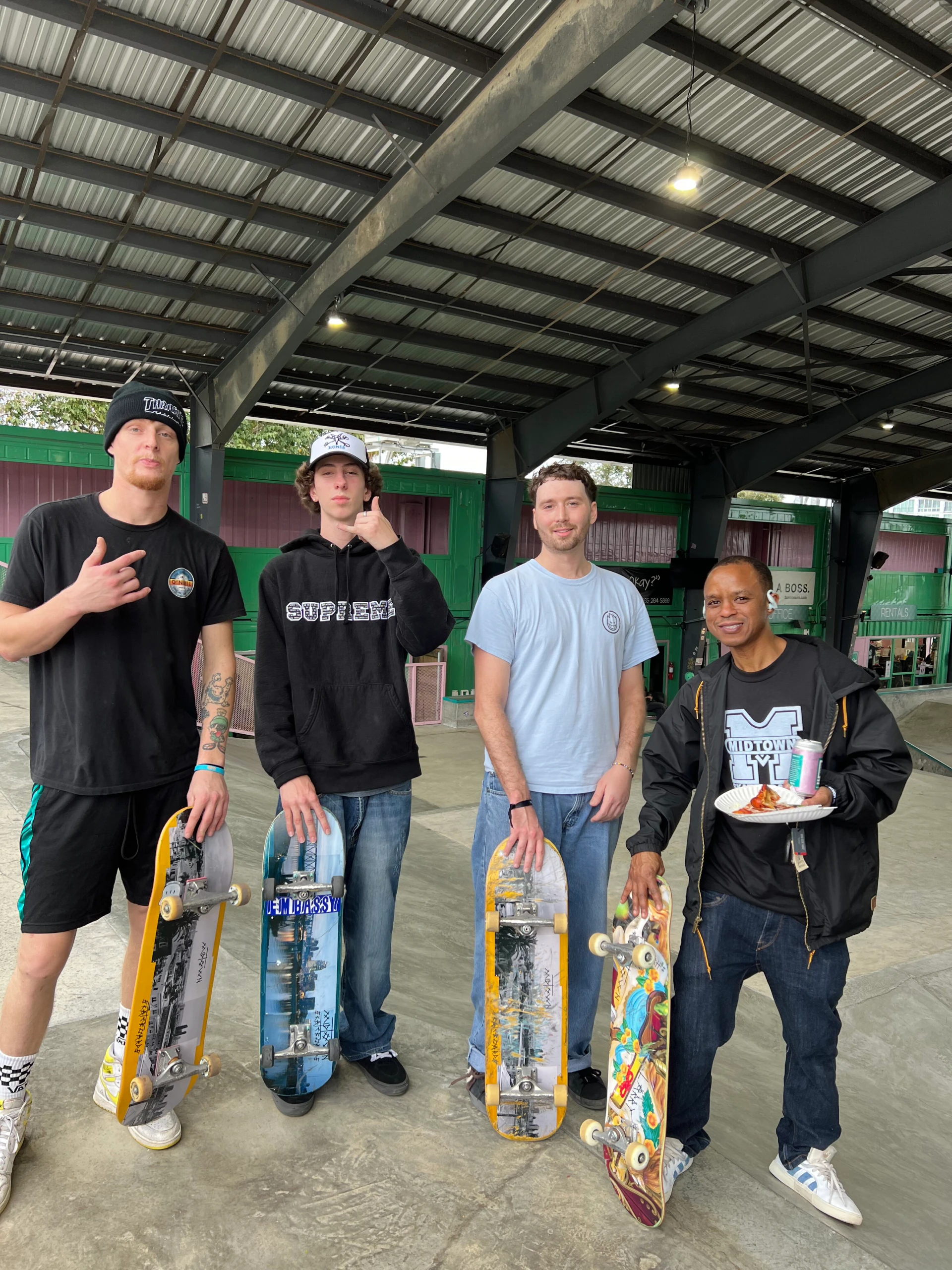 Group of four adult skateboarders posing inside skate park with their boards.