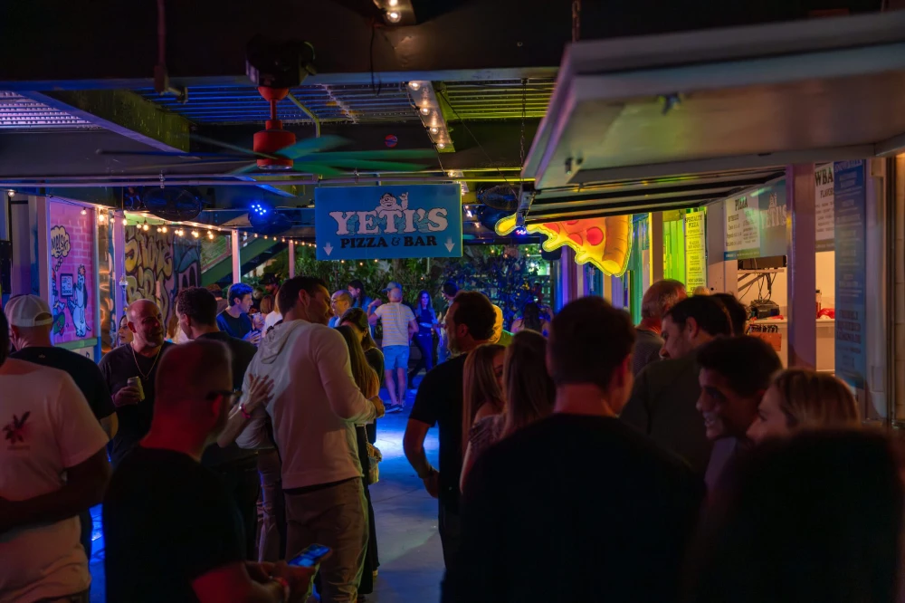 A crowd gathers at Yeti's Pizza Bar with colorful neon and string lights.