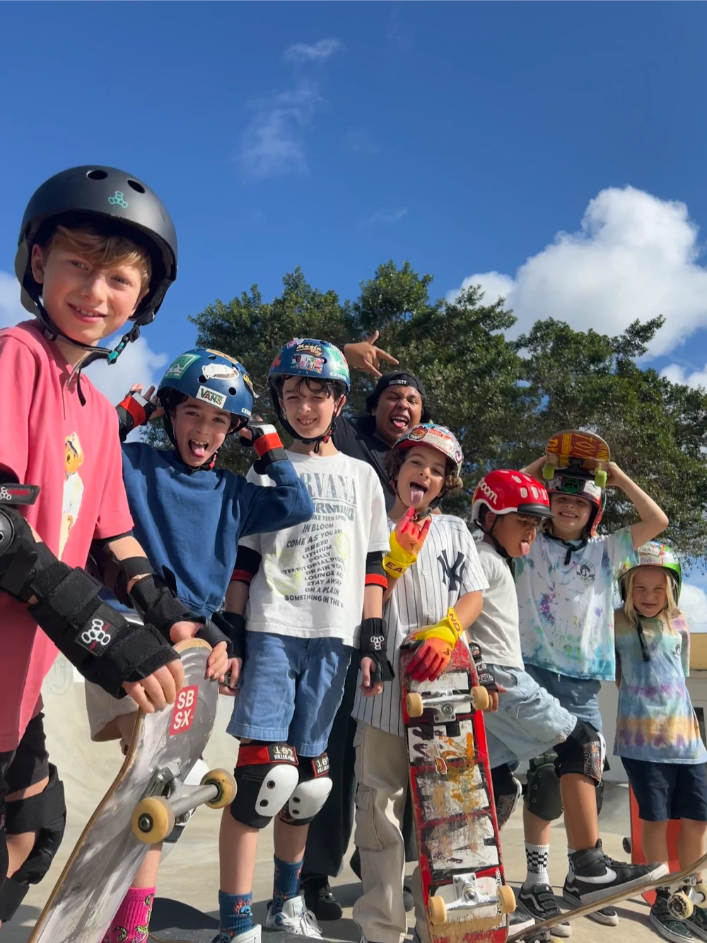 Smiling kids pose together with skateboards on a sunny day at the park.