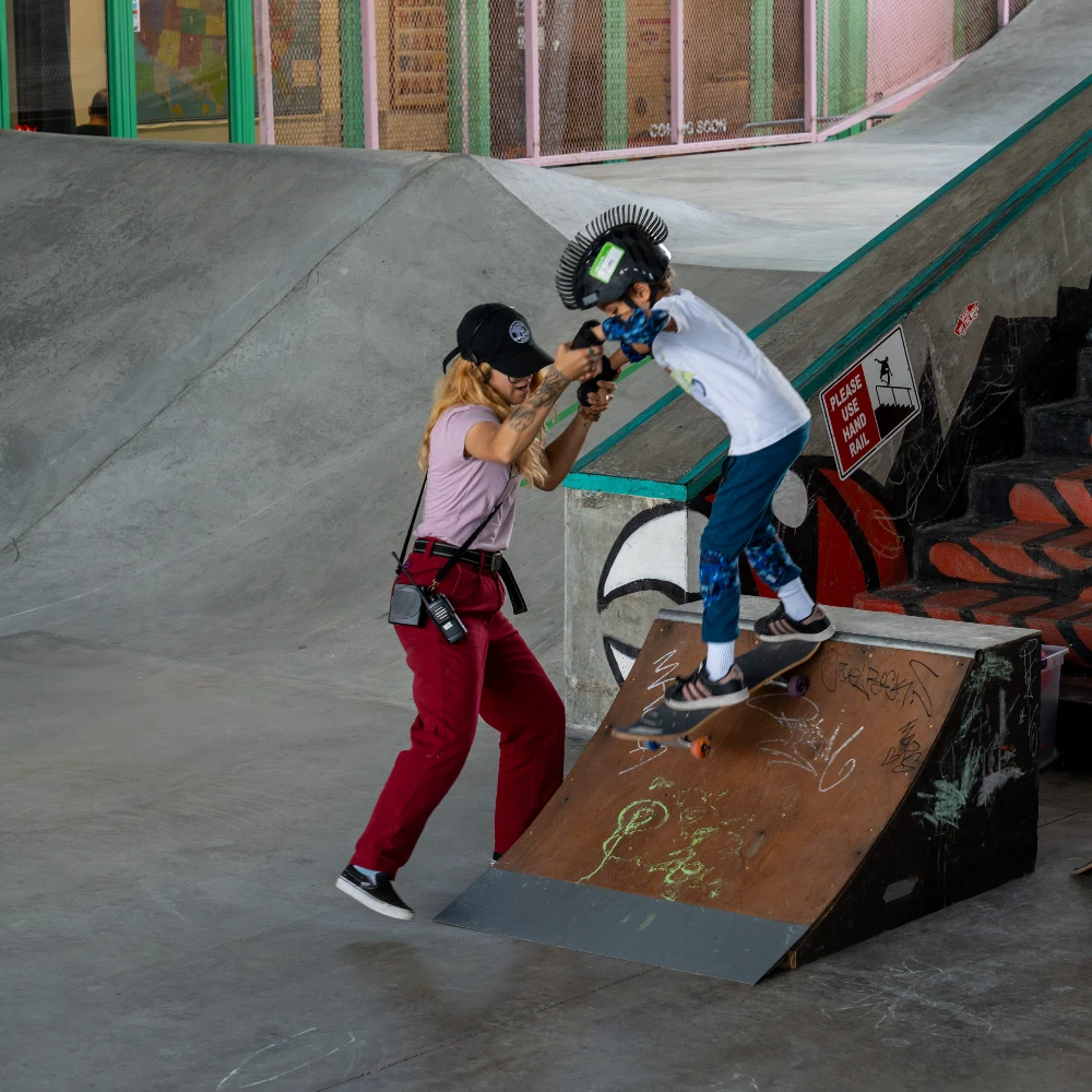 Instructor assists young child skateboarding down ramp with focused support.