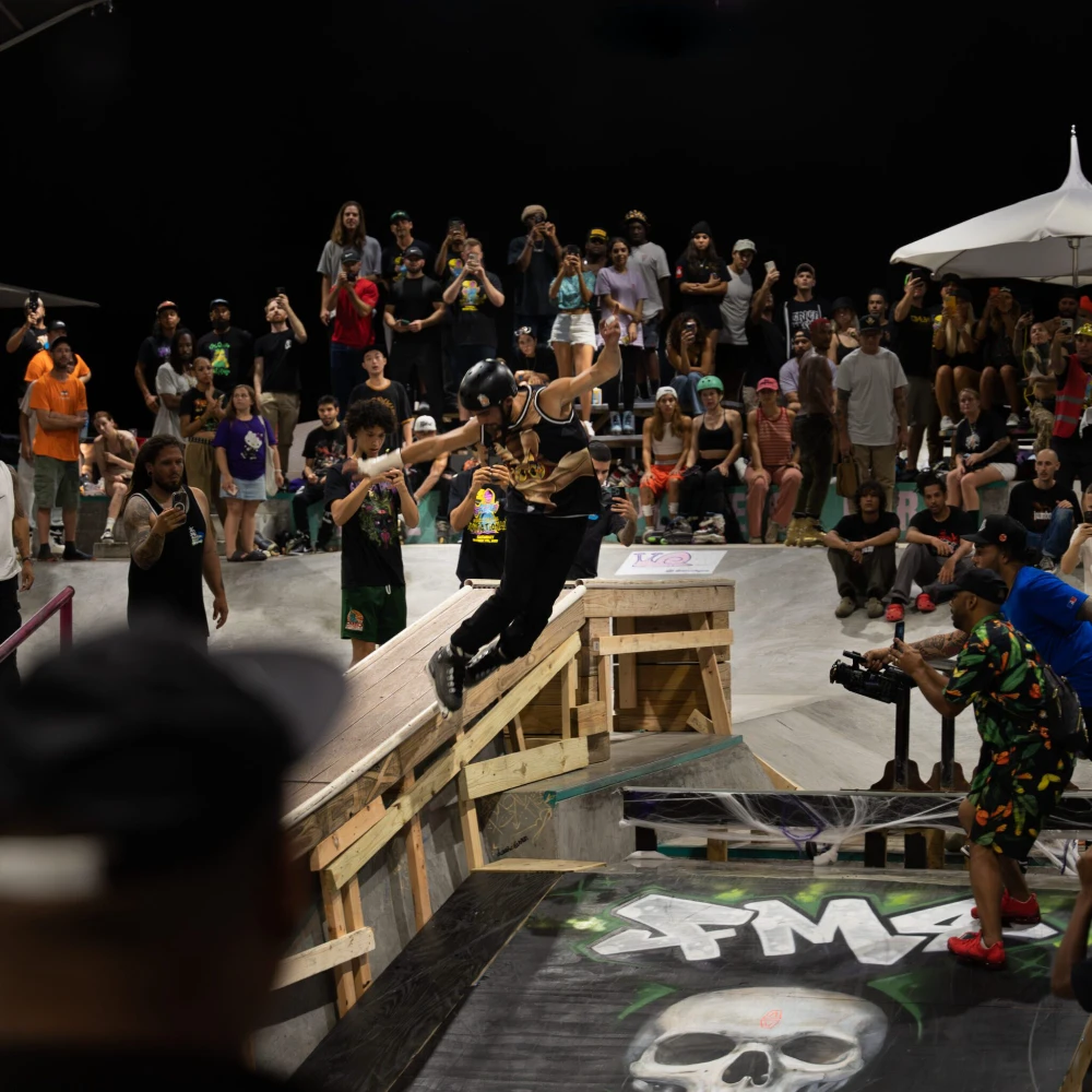 A skateboarder in mid-air performs a trick over a ramp for a crowd.
