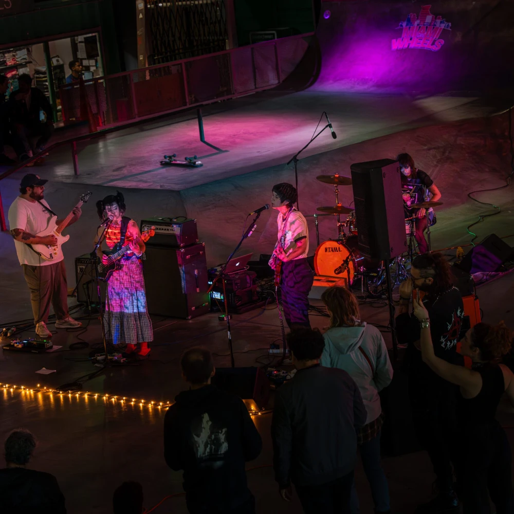A band performs with purple lighting at an indoor venue with an audience.