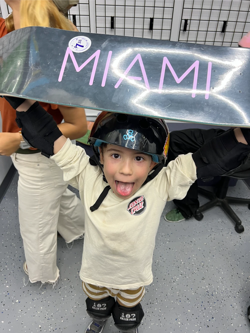 Excited young skateboarder holding a shiny deck labeled “MIAMI” over head.