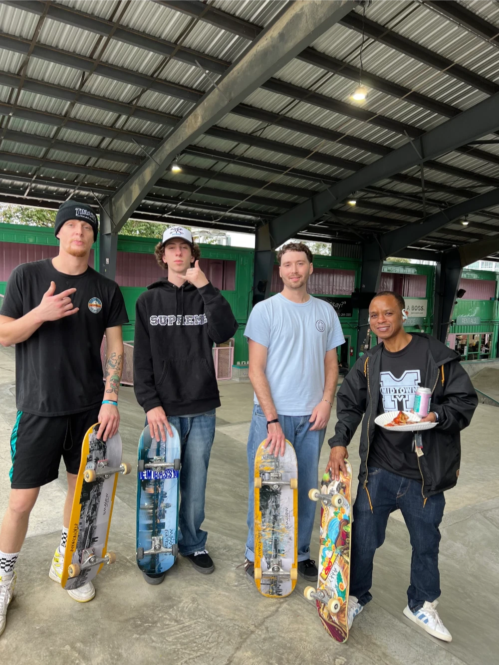 Group of four adult skateboarders posing inside skate park with their boards.