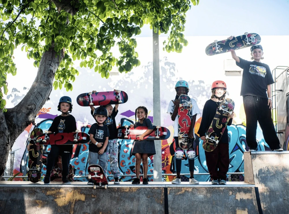 Group of kids proudly hold skateboards on ramp with colorful graffiti wall.