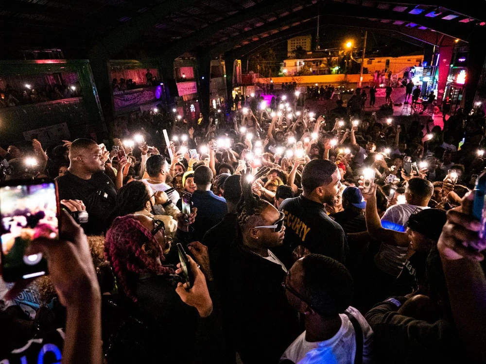 A large, excited crowd at a concert holds up their glowing phone lights.