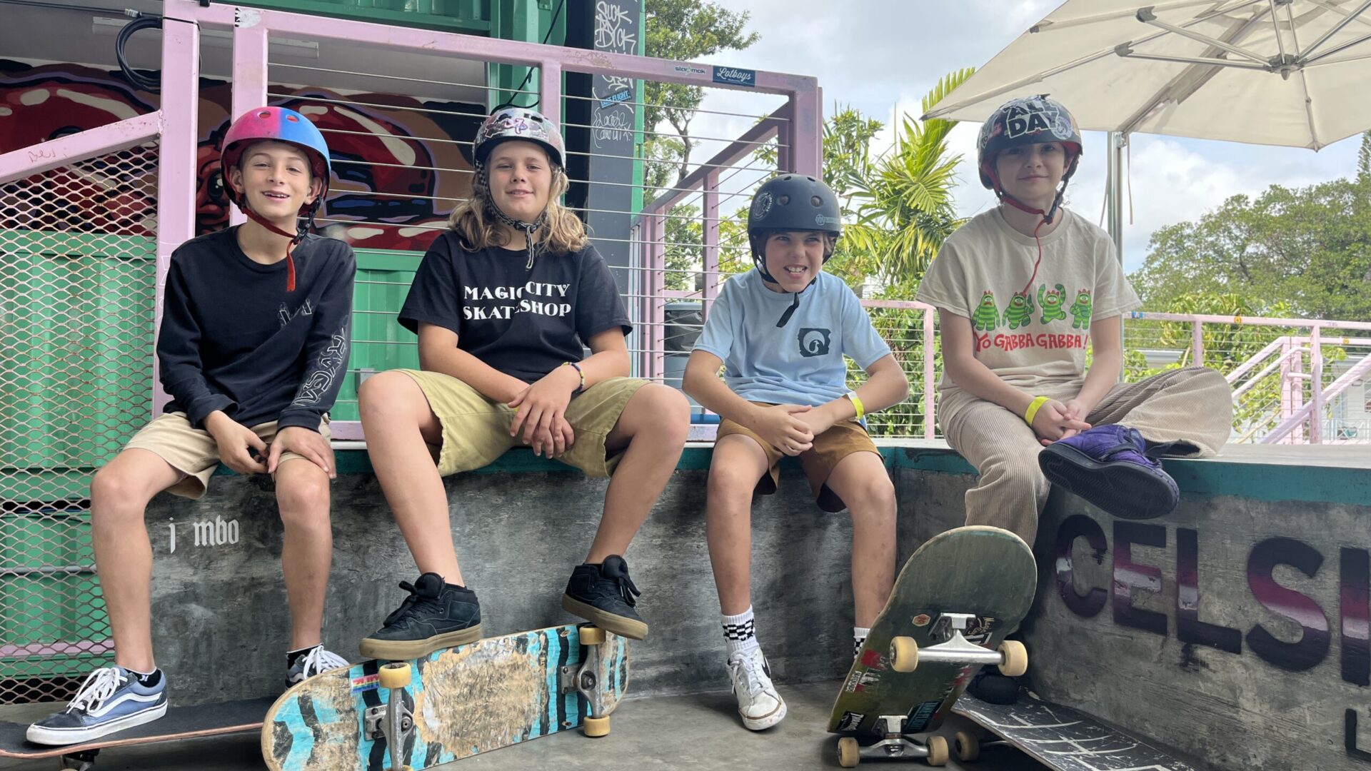 Four young skateboarders with helmets sit together on a ramp with their boards. Four young skateboarders with helmets sit together on a ramp with their boards.